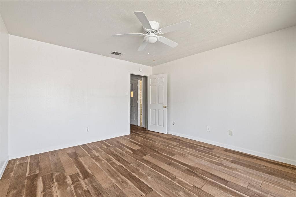 Interior room featuring wood-finish flooring, white walls, and a ceiling-mounted fan with integrated lighting