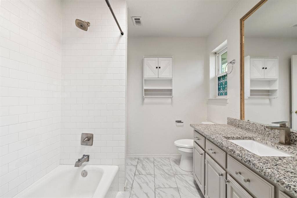 Bathroom featuring a white subway tile surround, stone-composite countertop, undermount sink, shaker-style vanity cabinetry, and patterned floor tile