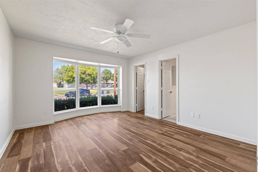 Interior space featuring wood-finish flooring, a multi-pane bay window, and a white ceiling fan with integrated lighting