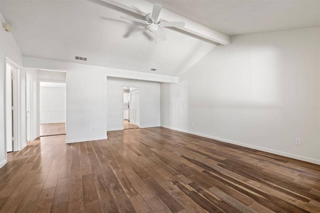 Vaulted ceiling with an exposed beam, wood-finish flooring, and a central ceiling fan