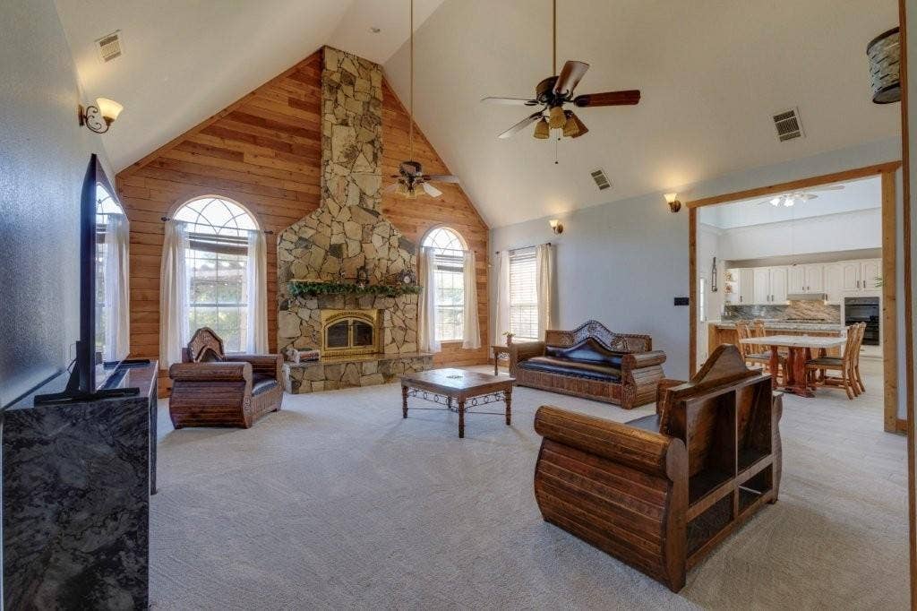 Vaulted ceiling featuring wooden accent wall, floor-to-ceiling stone fireplace with mantel, and arched windows