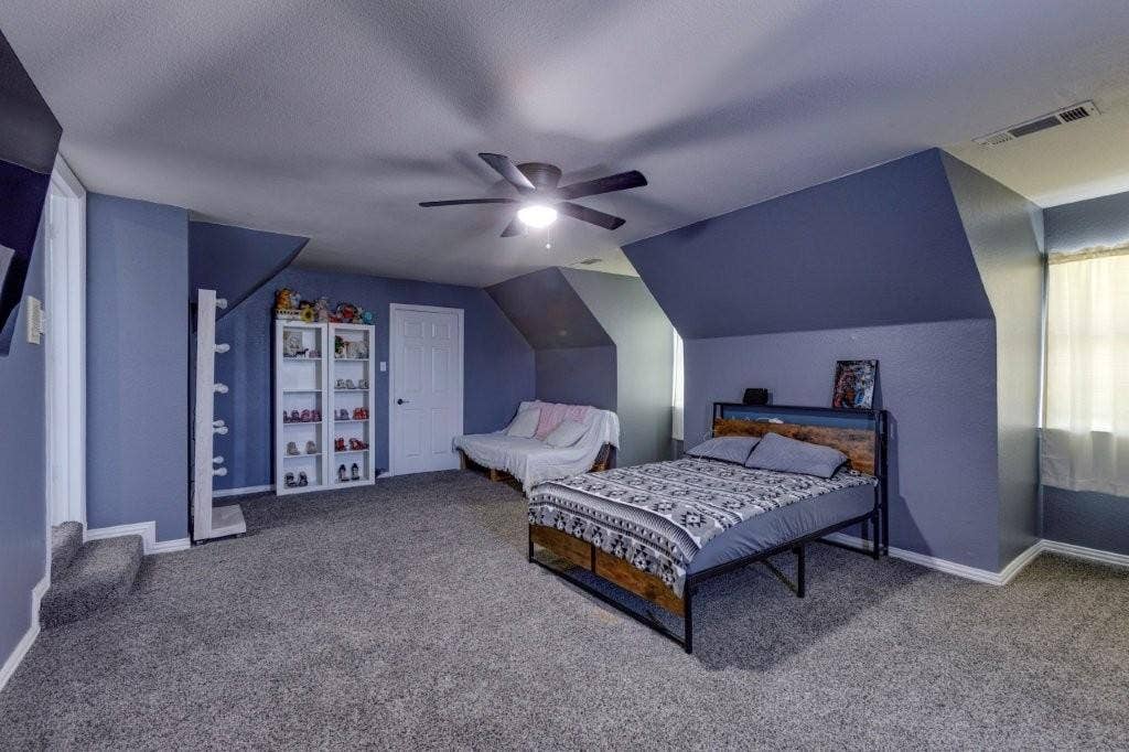 Spacious room featuring vaulted ceilings, neutral carpeting, and a ceiling fan with integrated lighting