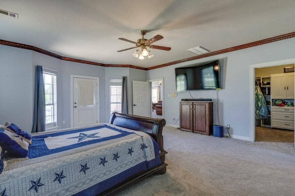 Spacious room featuring neutral carpeting, crown molding with decorative trim, a central ceiling fan with integrated lighting, and a built-in closet with cabinetry