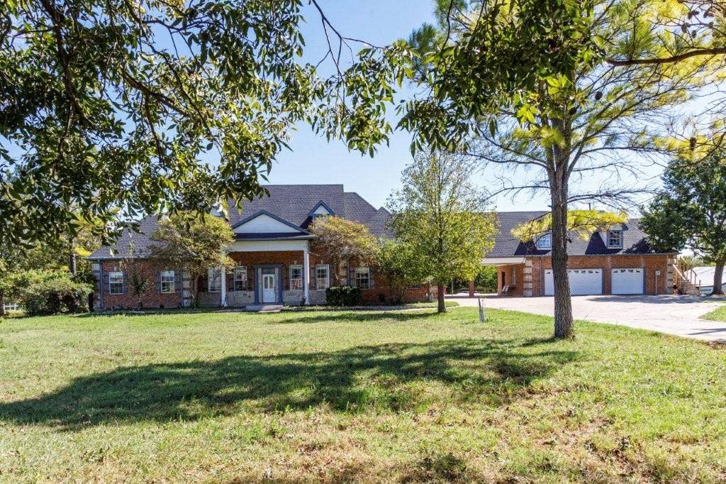 Traditional brick exterior featuring a covered front porch, multi-gabled roofline, and attached three-car garage situated on a sprawling lot with mature trees