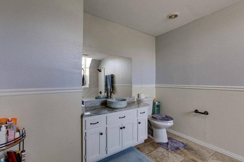 White vanity with stone-patterned countertop, vessel sink, large wall-mounted mirror, and tile flooring