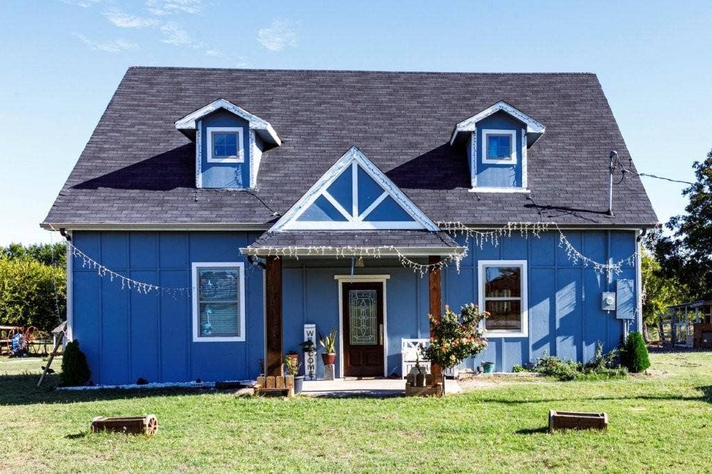 Two-story board and batten exterior featuring a central gable roofline, two roof dormers, a covered front porch with timber posts, and an architectural glass-panel entry door