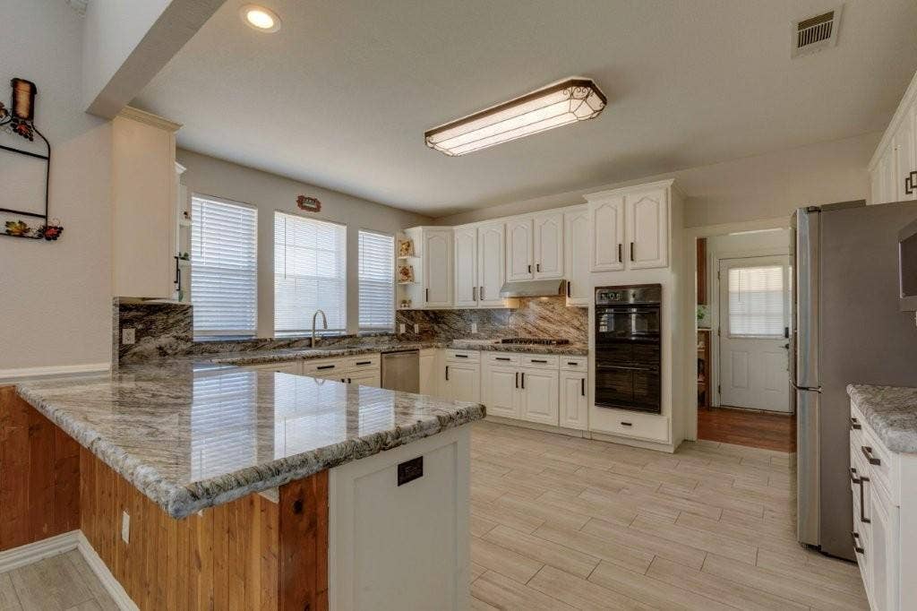 Kitchen featuring white cabinetry, stone countertops, integrated stainless steel oven, wood-panelled island base, and tile flooring
