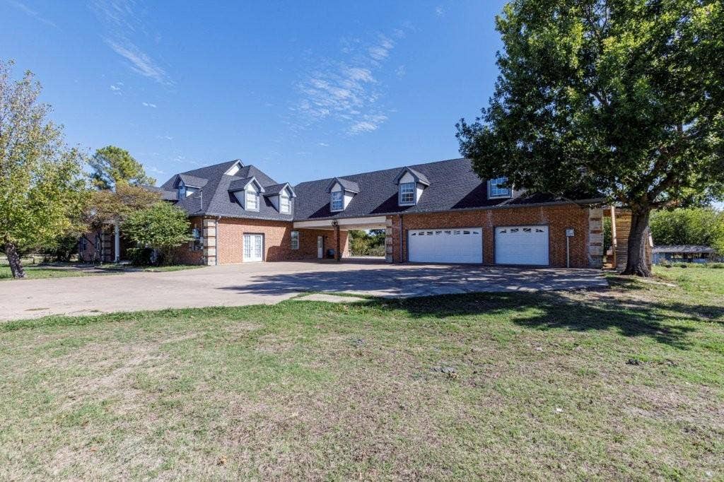 Brick exterior with multi-gabled roofline, dormer windows, attached two-car garage, and expansive concrete motor court