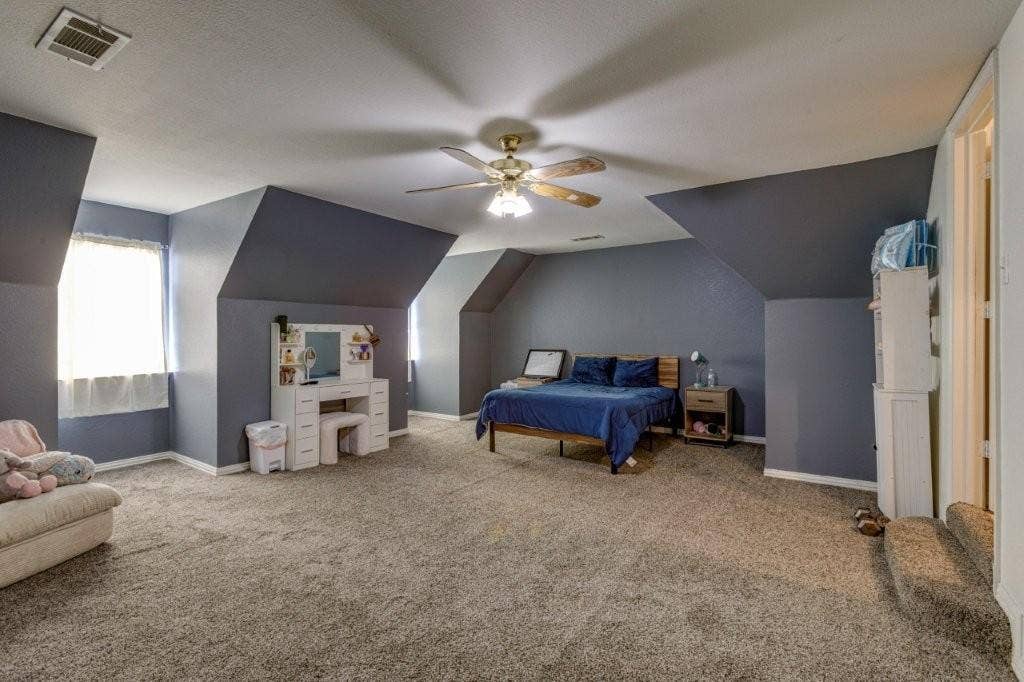 Expansive room featuring vaulted ceilings, neutral carpeting, multi-pane windows, and a ceiling fan with integrated lighting