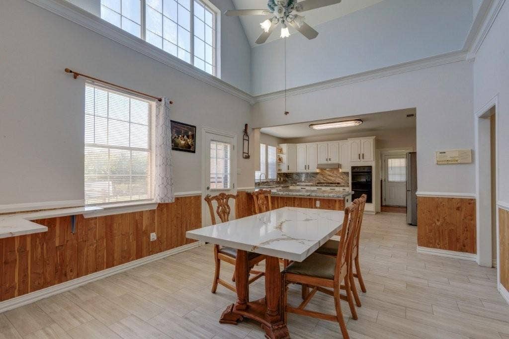 Vaulted ceiling featuring a clerestory window and ceiling fan, wood-panel wainscoting, and ceramic tile flooring