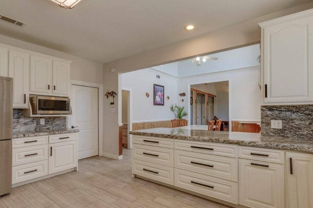 Kitchen featuring white cabinetry, stone-finish countertops, matte black hardware, built-in microwave, and wood-finish tile flooring