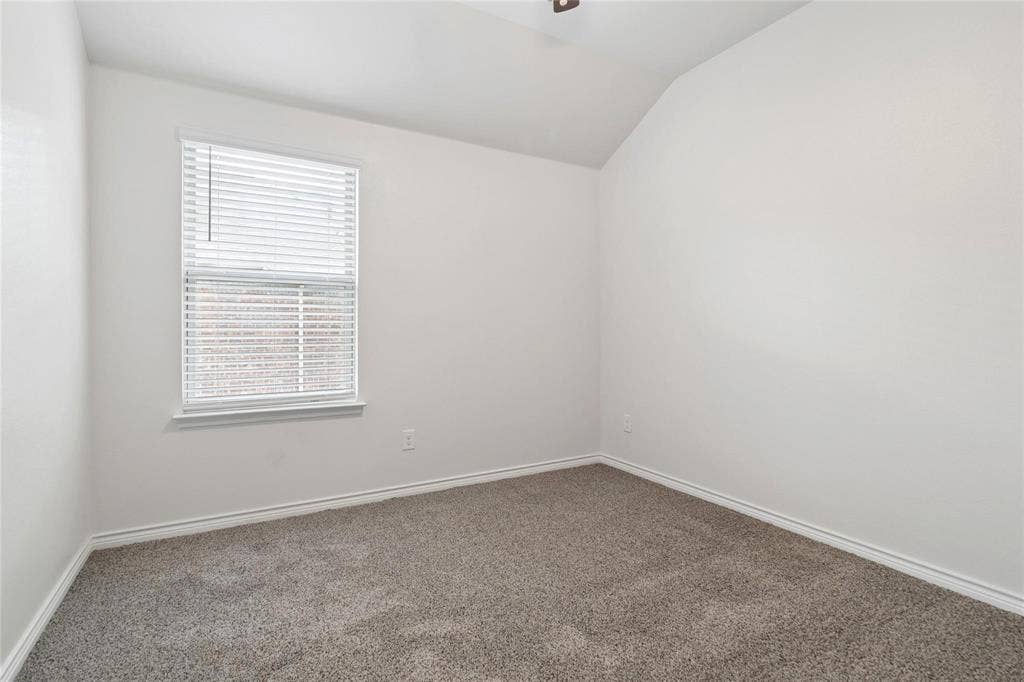 Neutral-toned room featuring a vaulted ceiling, wall-to-wall carpeting, and a window with horizontal blinds