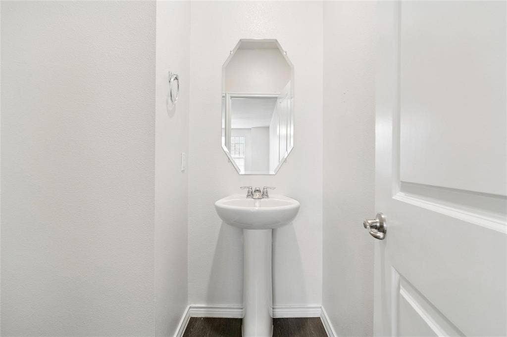 Pedestal sink with chrome dual-handle faucet, octagonal wall-mounted mirror, and wood-finish flooring