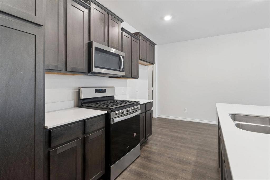 Kitchen featuring dark-finish cabinetry, quartz countertops, stainless steel gas range, built-in microwave, and wood-finish flooring