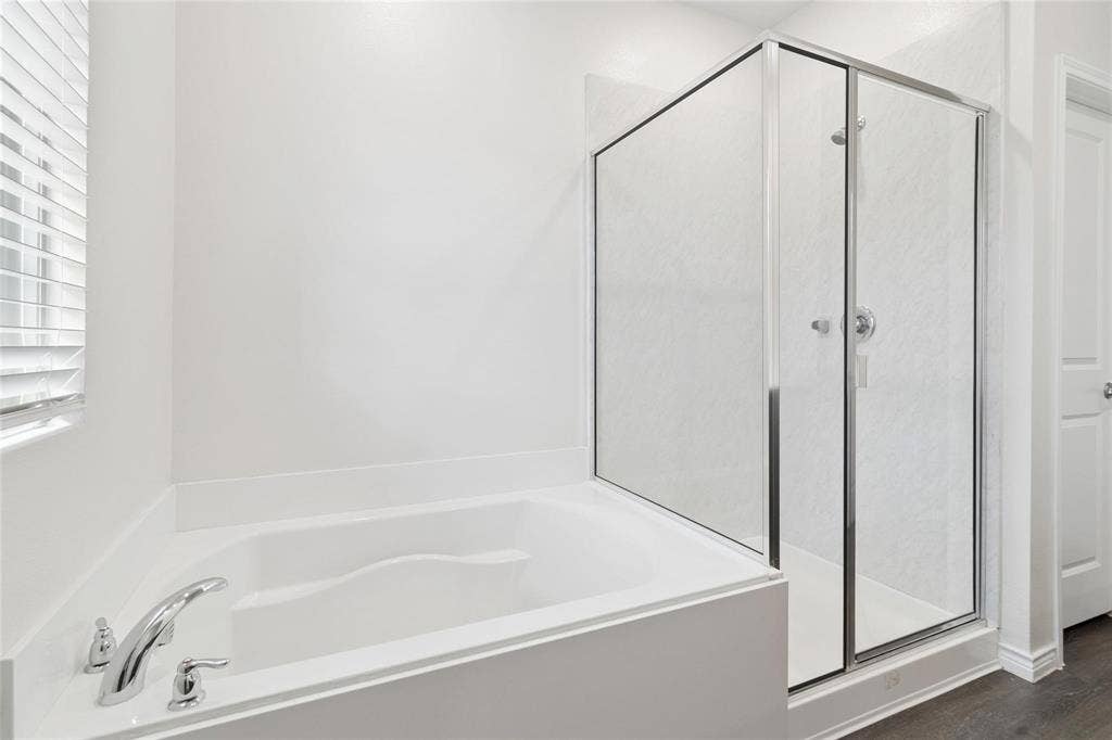 Soaking tub with chrome faucet fixture, glass-enclosed shower, and wood-finish flooring