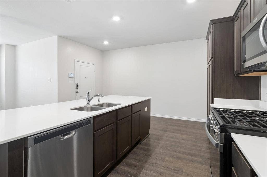 Kitchen featuring dark-finish cabinetry, white countertops, stainless steel dual-basin sink, gas range, and wood-finish flooring