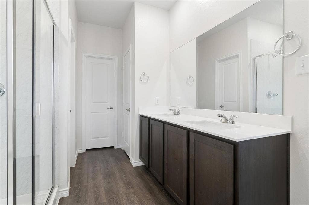 Dual-sink vanity with dark cabinetry and white countertop, full-width wall mirror, and walk-in shower with glass enclosure