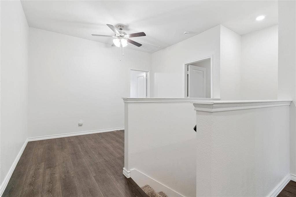 Neutral-toned interior space featuring wood-finish flooring, a ceiling fan with integrated light fixture, recessed lighting, and a half-wall partition with crown molding