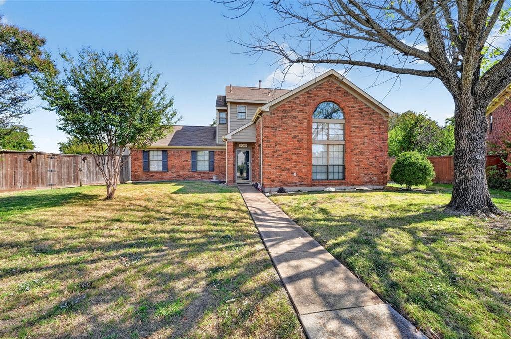 Multi-story brick exterior featuring a prominent arched window, shingle roofing, and a concrete walkway