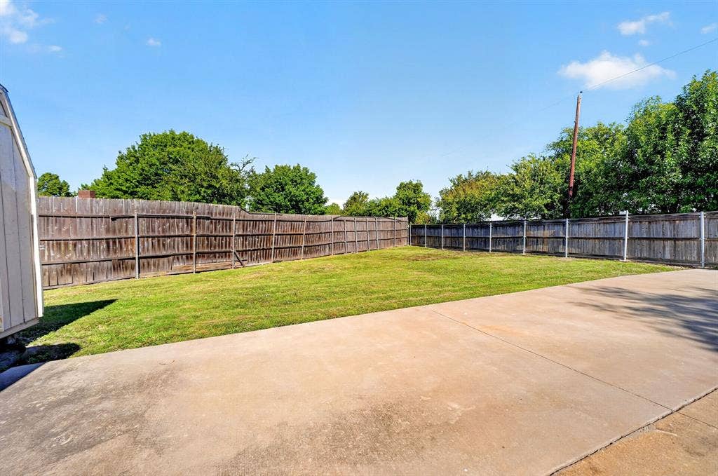 Expansive backyard featuring a concrete patio, level lawn, and perimeter wood fencing