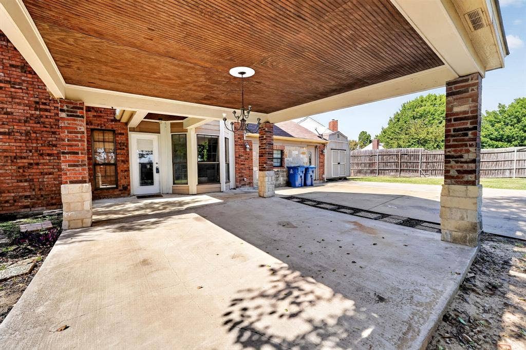 Covered patio featuring a wood-plank ceiling, brick and stone masonry pillars, and an attached chandelier