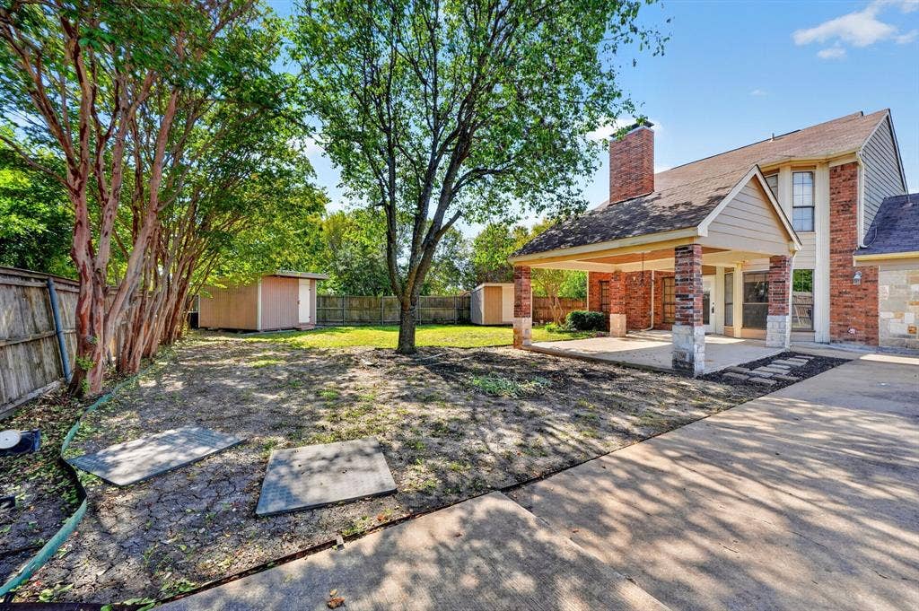 Backyard featuring a covered patio, brick masonry exterior, stone-accented support columns, and detached storage structures