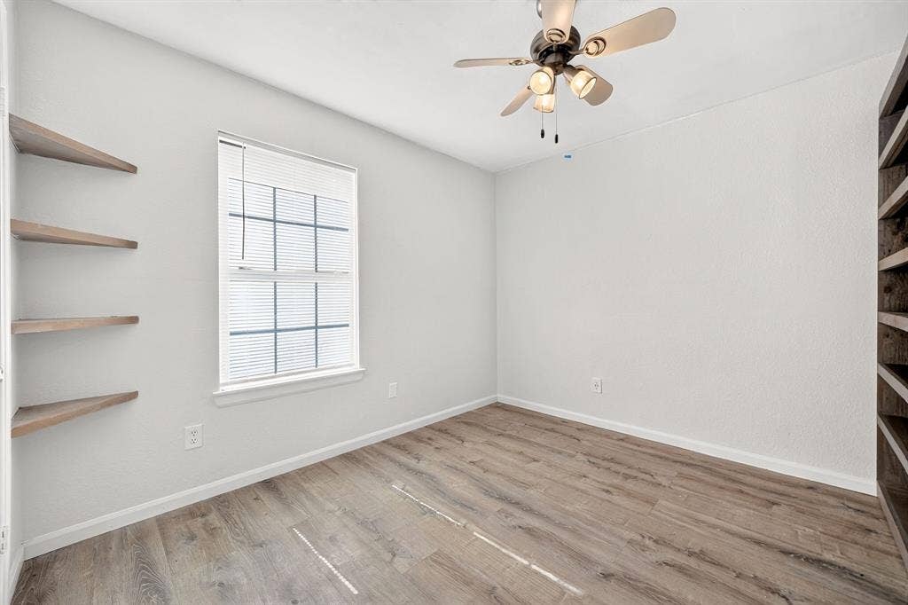 Wood-finish flooring, multi-pane window, built-in wooden corner shelving, floor-to-ceiling built-in wooden bookcase, and ceiling fan with integrated lighting