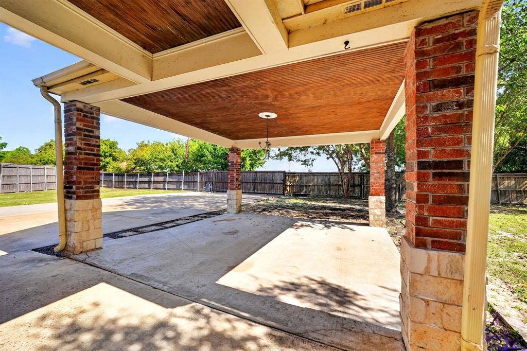 Covered patio featuring a wood-paneled ceiling, brick and stone masonry columns, and a concrete foundation