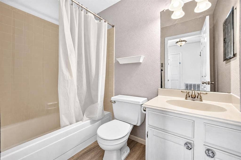 Bathroom featuring a white vanity with a neutral solid-surface countertop, an integrated oval sink, a wall-to-wall mirror, and wood-finish flooring