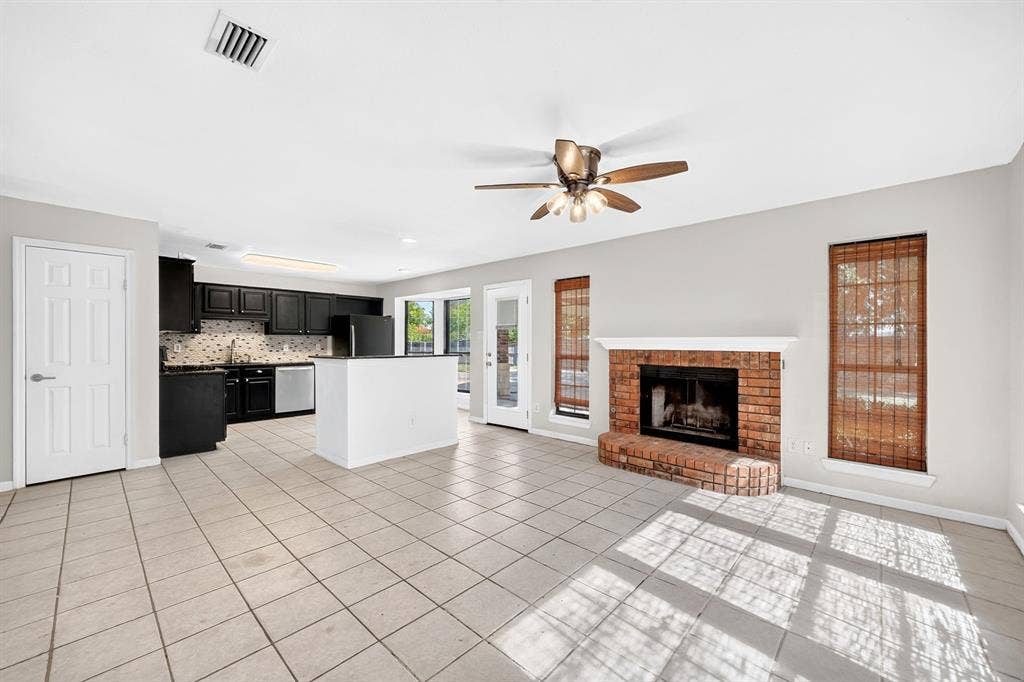 Kitchen featuring dark cabinetry, solid-surface island, and built-in appliances, paired with a living area showcasing a brick fireplace and tile flooring