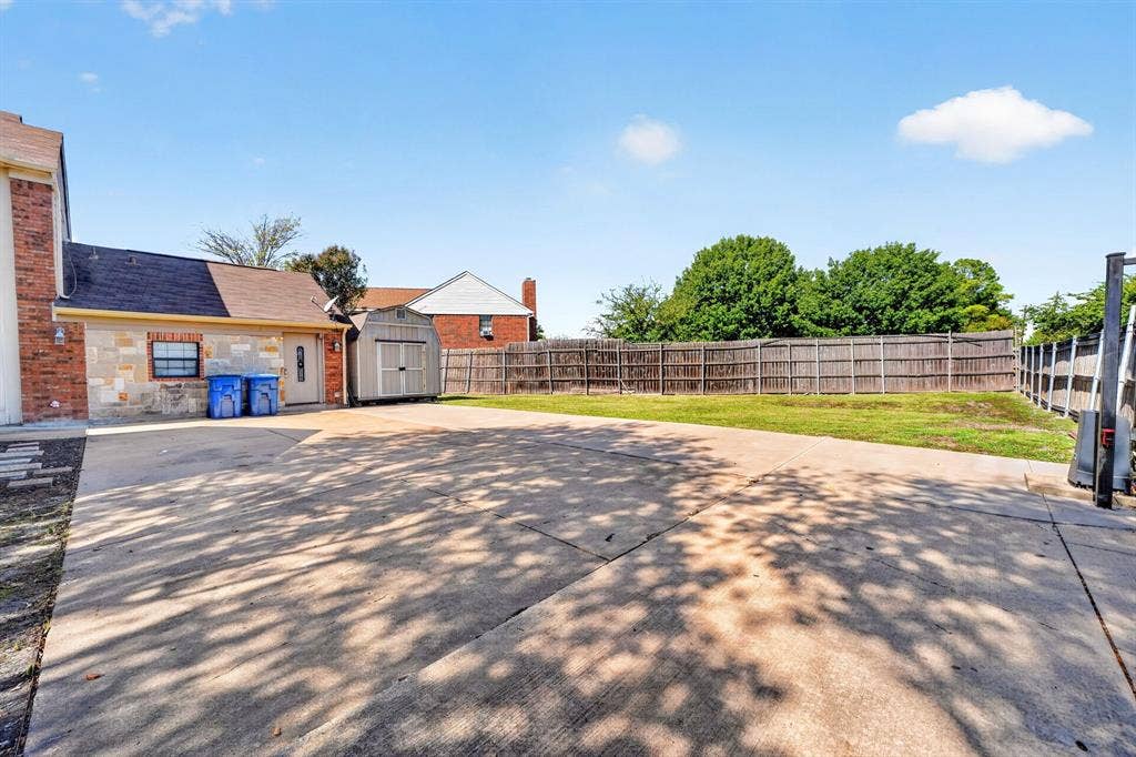 Expansive concrete driveway, fenced backyard with a manicured lawn, and an exterior storage shed