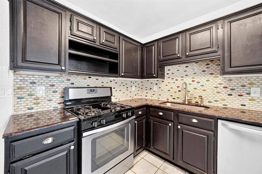 Kitchen featuring dark finish cabinetry, stone countertops, stainless steel gas range, multi-colored brick-pattern tile backsplash, and stainless steel under-mount sink with gooseneck faucet