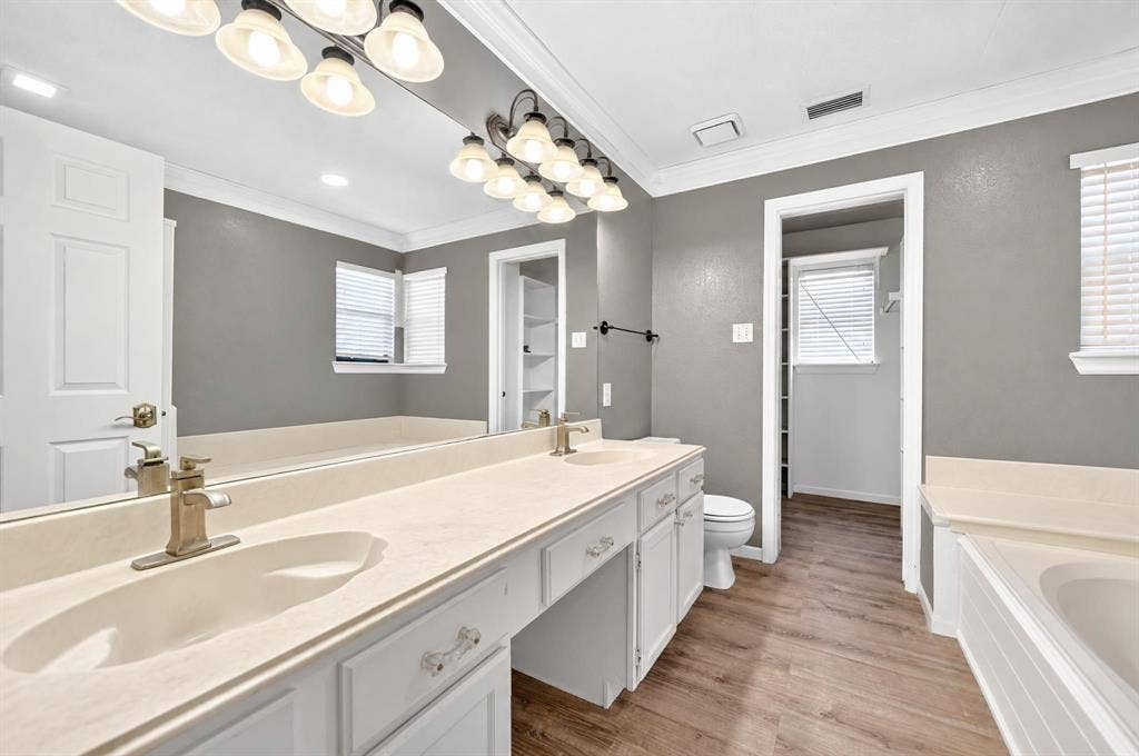Dual-sink vanity with solid surface countertop, wood-finish flooring, full-width wall mirror, and integrated soaking tub