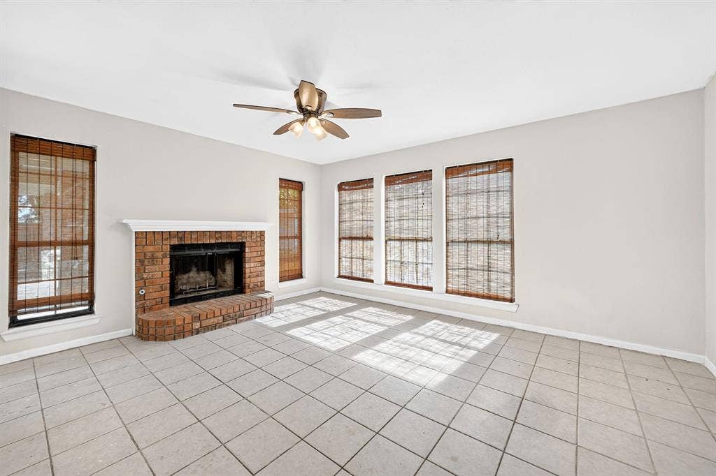 Brick fireplace with a raised hearth, large-format tile flooring, and a ceiling fan with integrated lighting