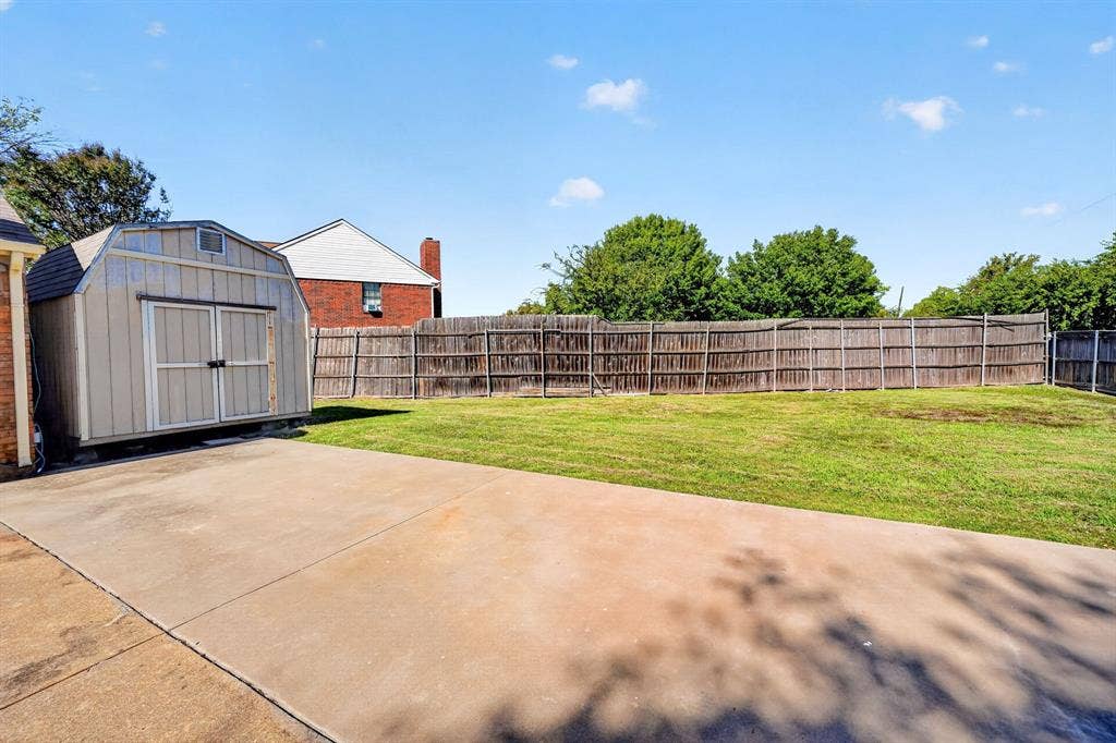 Backyard storage building and featuring a concrete patio, grassy lawn, wood privacy fencing, and an exterior storage shed
