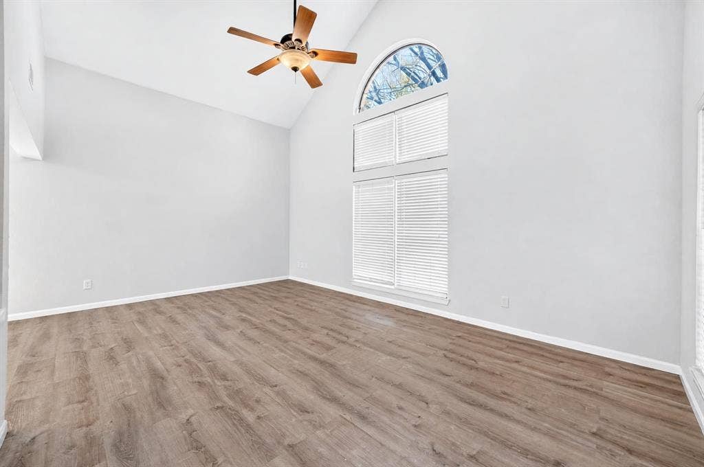 Vaulted ceiling featuring an arched window, wood-finish flooring, and a ceiling fan with integrated lighting