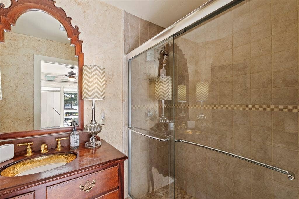 230 Bushwhacker Drive, Mabank, TX 75156 Bathroom featuring a wood vanity with a recessed basin, gold-tone faucet hardware, arched wall mirror, and a walk-in shower enclosure with tile surround