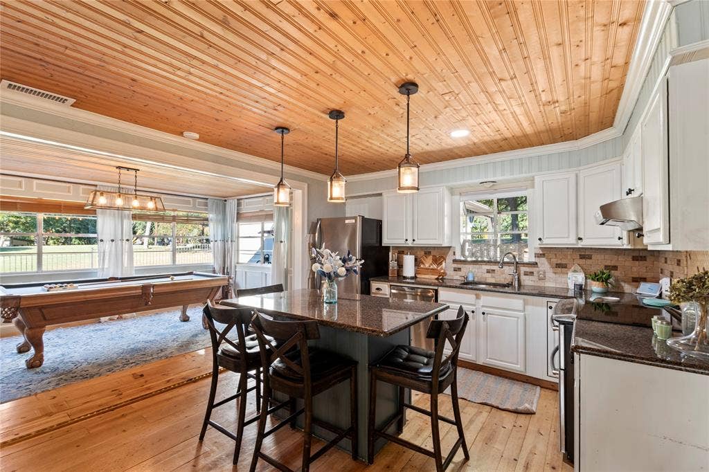 230 Bushwhacker Drive, Mabank, TX 75156 Kitchen featuring wood-plank ceiling, natural wood-finish flooring, white cabinetry, dark stone countertops, and three pendant lights over a central island