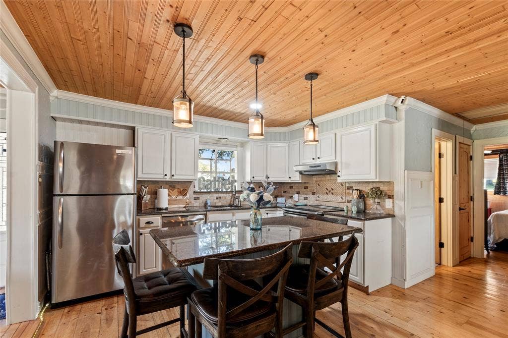 230 Bushwhacker Drive, Mabank, TX 75156 Kitchen featuring natural wood-plank ceiling, white cabinetry, central island with stone countertop, stainless steel refrigerator, and three pendant light fixtures