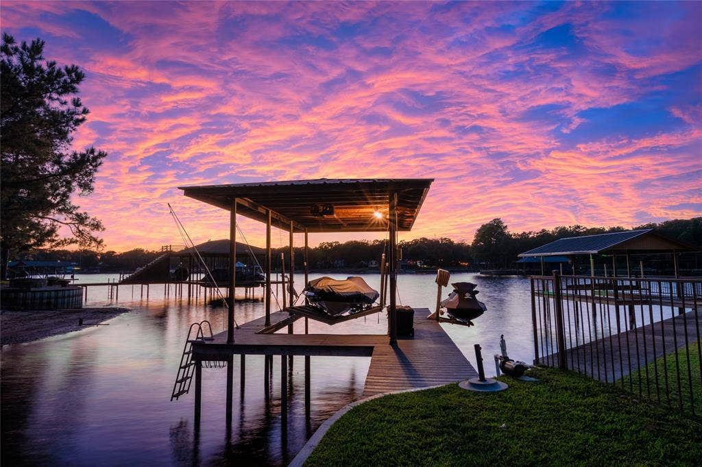 230 Bushwhacker Drive, Mabank, TX 75156 Waterfront property featuring a private covered boat dock, fixed pilings, metal roof structure, and metal perimeter fencing