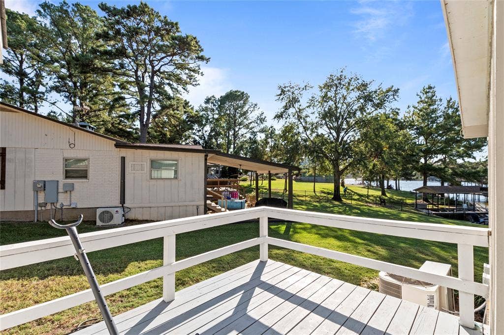 230 Bushwhacker Drive, Mabank, TX 75156 Elevated deck with white horizontal railing overlooking a grass lawn, mature trees, and waterfront access with a private pier