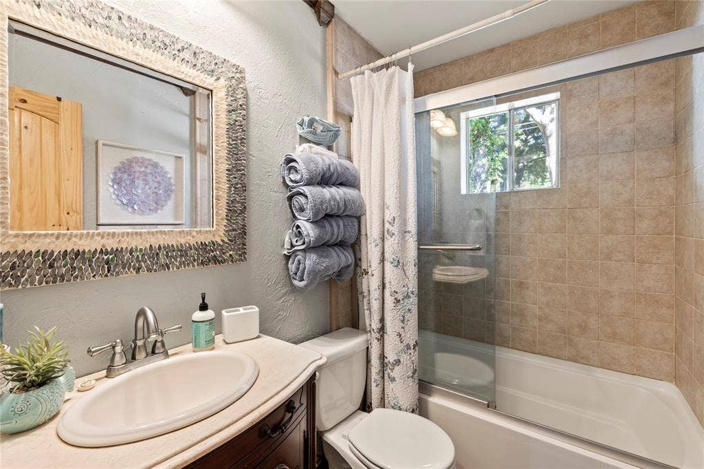 230 Bushwhacker Drive, Mabank, TX 75156 Bathroom featuring a vanity with a drop-in sink, a wall-mounted mirror with mosaic tile trim, and a bathtub-shower combination with a sliding glass door and tiled surround