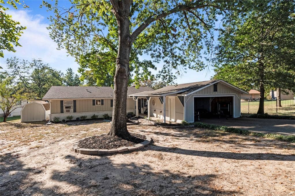 230 Bushwhacker Drive, Mabank, TX 75156 Single-story exterior featuring vertical siding, attached carport, detached storage shed, and stone tree surround