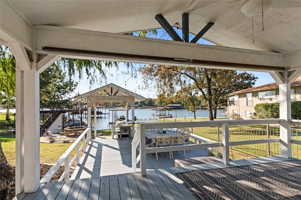230 Bushwhacker Drive, Mabank, TX 75156 Covered outdoor patio featuring a vaulted ceiling, ceiling fan, and painted wood decking, leading to a wooden dock structure on the water