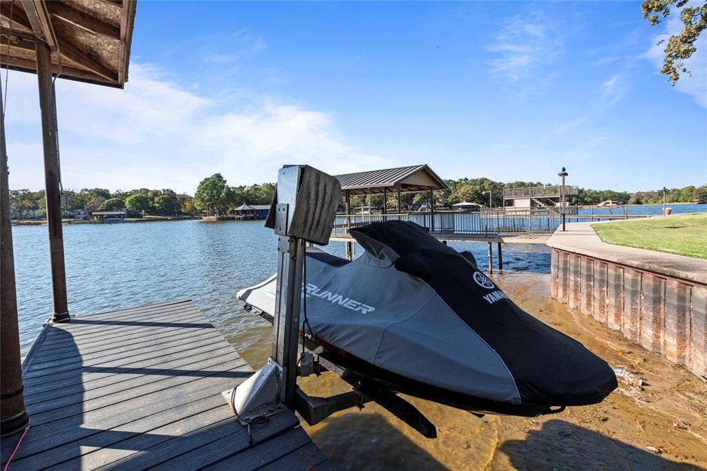 230 Bushwhacker Drive, Mabank, TX 75156 Private wooden dock featuring a mechanical personal watercraft lift, covered boat slip, steel bulkhead, and concrete shoreline path