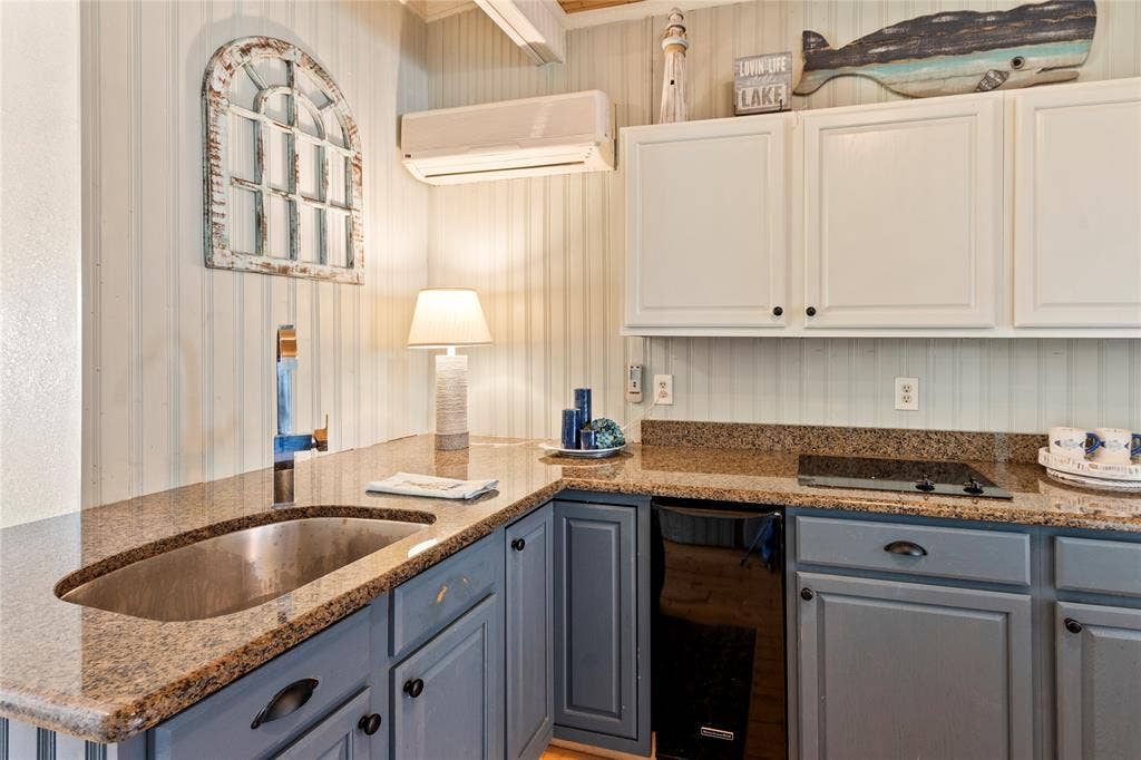 230 Bushwhacker Drive, Mabank, TX 75156 Kitchen area featuring two-tone cabinetry, stone-finish countertops, stainless steel undermount sink with a gooseneck faucet, vertical paneled wall treatments, and an integrated wall-mounted ductless climate control unit