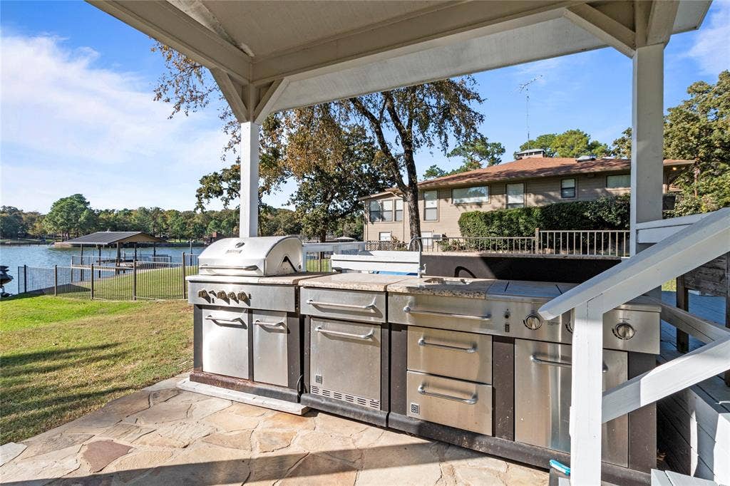 230 Bushwhacker Drive, Mabank, TX 75156 Covered patio featuring an outdoor kitchen with stainless steel grill, stone-surfaced countertop, integrated sink, and flagstone flooring