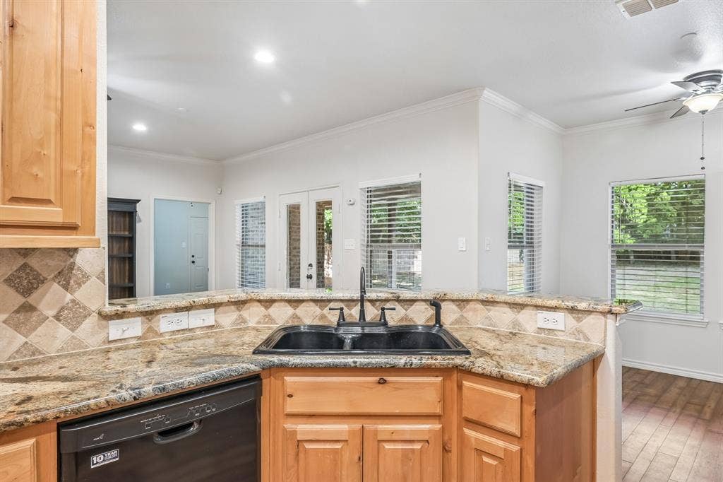Kitchen featuring wood cabinetry, a double basin sink with a black faucet, and granite countertops with a tile backsplash
