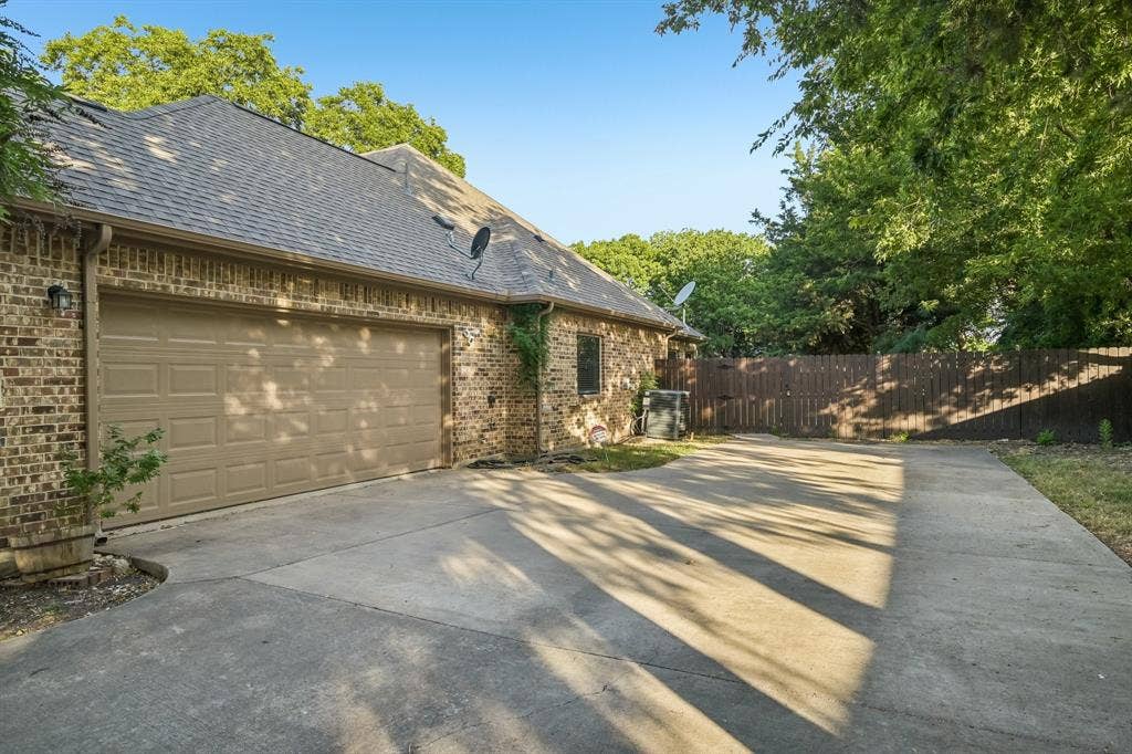 Brick exterior with a multi-car concrete driveway, attached garage, and a privacy fence