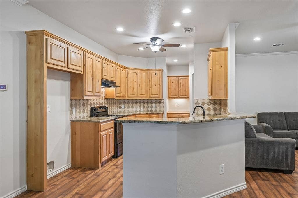 Kitchen featuring wood-finish cabinetry, patterned tile backsplash, recessed lighting, and a breakfast bar with a stone-finish countertop